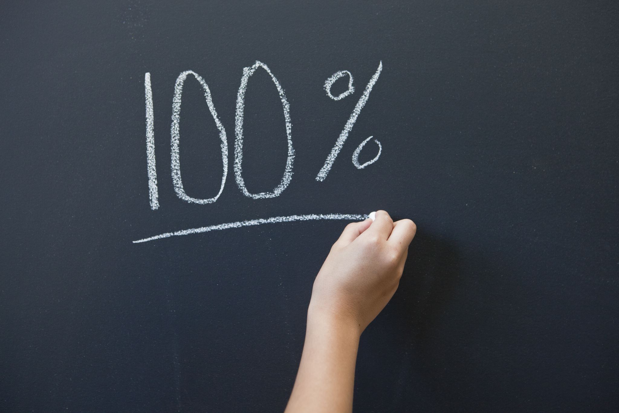 A child writing the word 100% on a blackboard