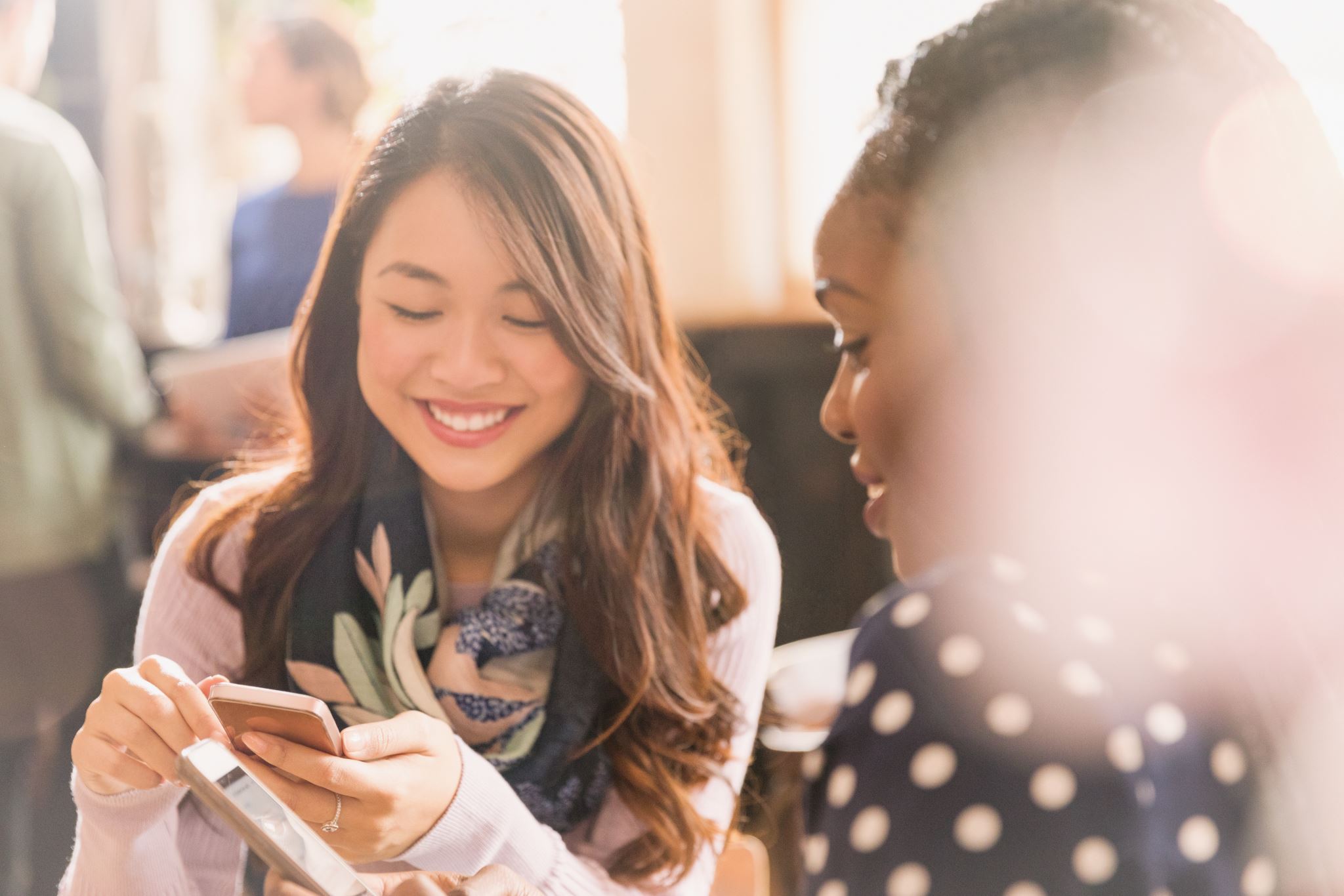 Female friends texting with cell phones in cafe